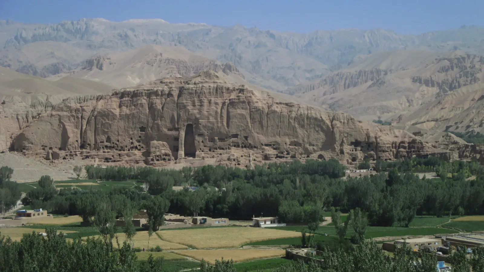 Bamiyan cliff with the empty niche of a destroyed monumental Buddha above the cultivated valley.