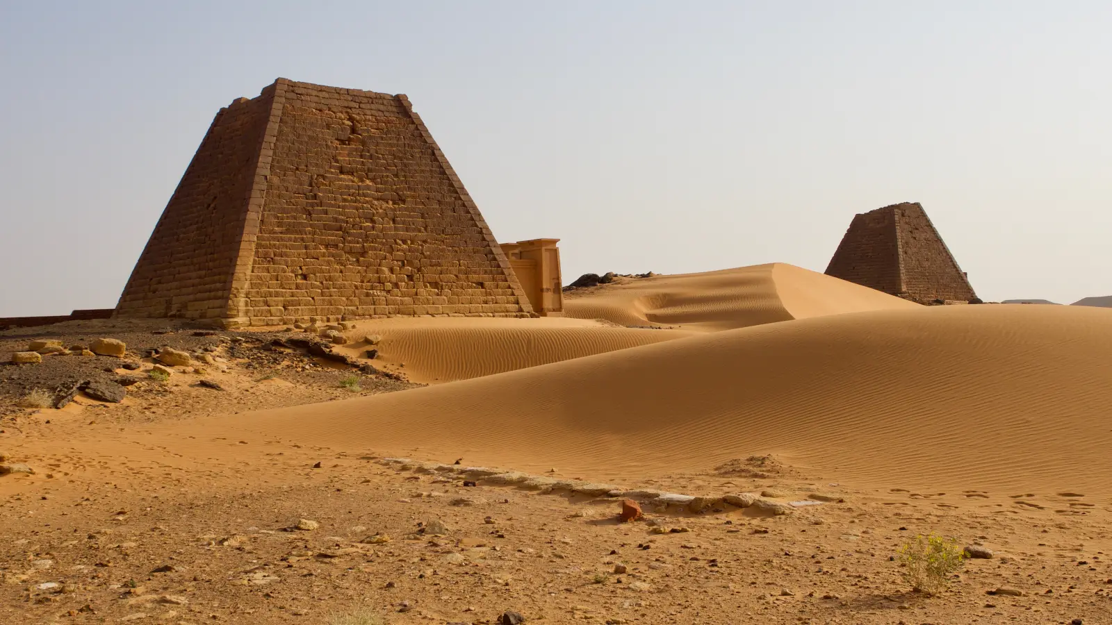 Steep-sided Kushite pyramids rising among wind-shaped dunes at Meroë in Sudan.