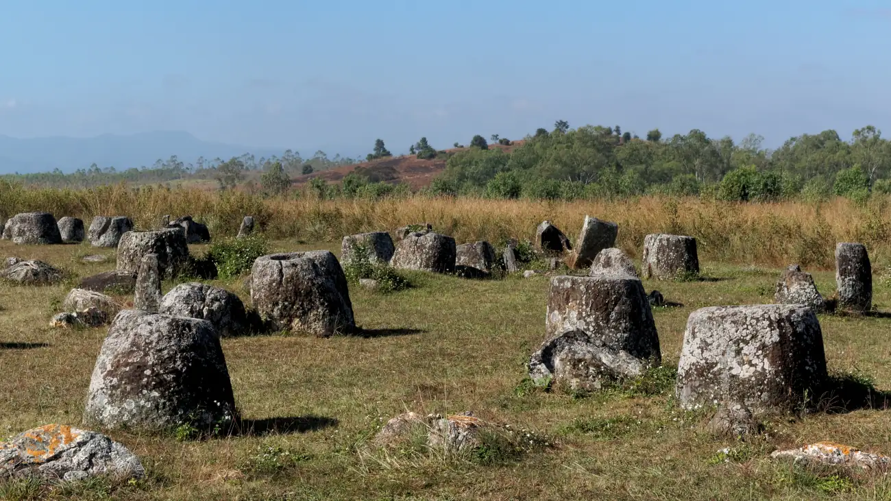 Groups of large carved stone jars scattered across grassland on the Plain of Jars in Laos.