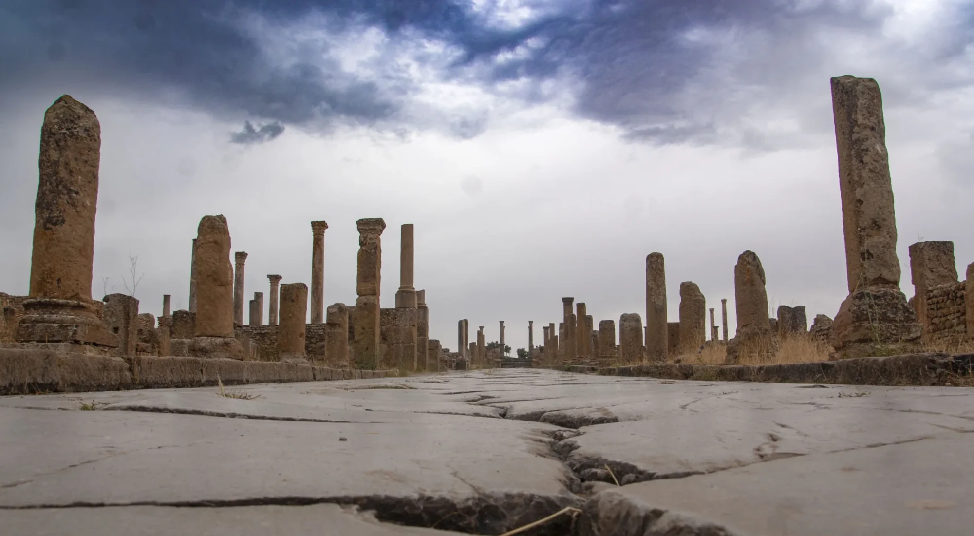The paved Roman street and standing columns at Timgad beneath a cloudy sky